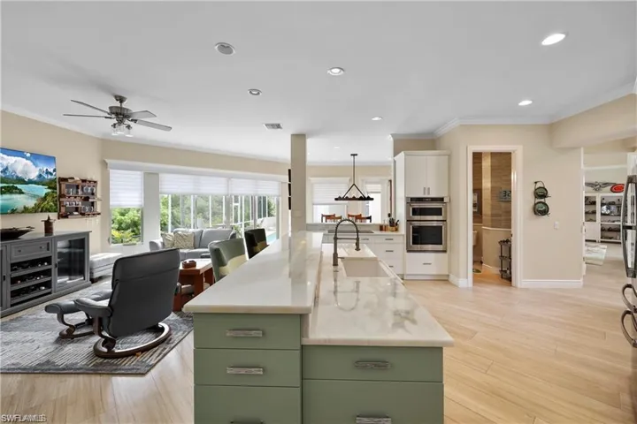 Kitchen with hanging light fixtures, light hardwood / wood-style floors, light stone counters, a kitchen island with sink, and sink