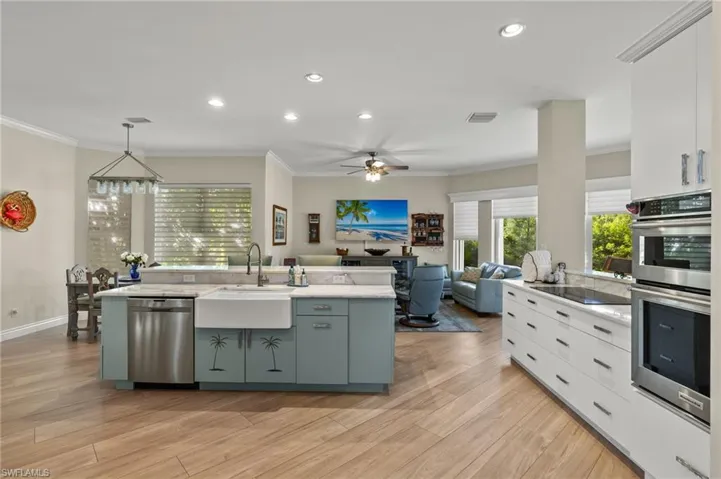 Kitchen featuring appliances with stainless steel finishes, light hardwood / wood-style floors, white cabinetry, decorative light fixtures, and a kitchen island with sink