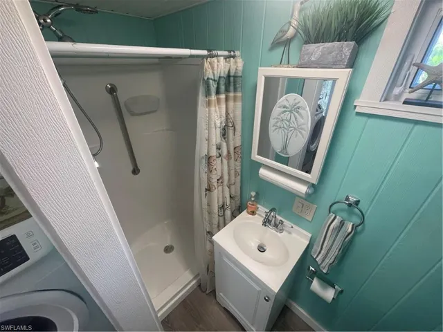 Bathroom featuring a stall shower, vanity, washer / clothes dryer, and wood walls