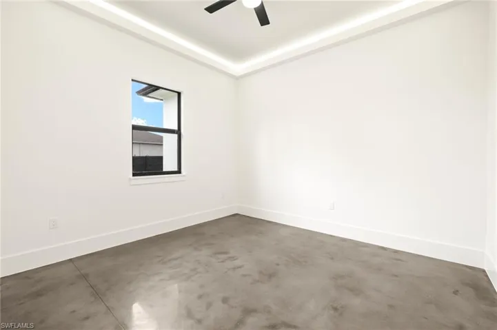 Unfurnished room with a raised ceiling, concrete flooring, ceiling fan, and baseboards