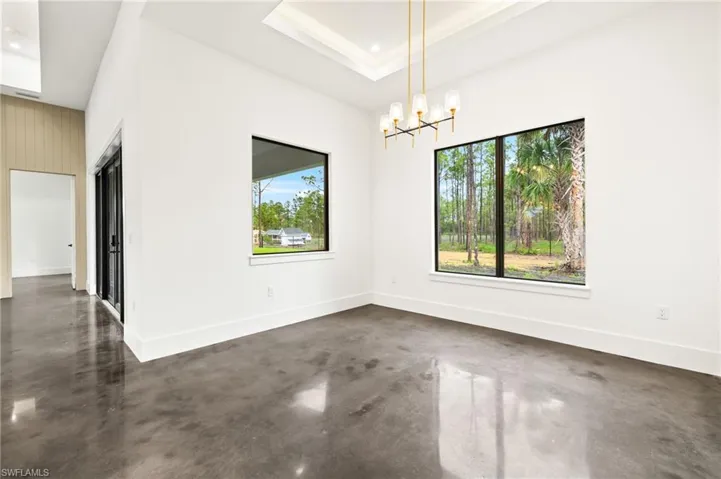 Spare room with baseboards, a notable chandelier, concrete flooring, a tray ceiling, and recessed lighting