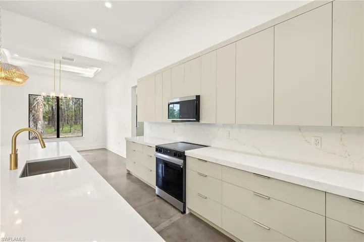 Kitchen with modern cabinets, tasteful backsplash, light stone counters, a sink, and stainless steel appliances