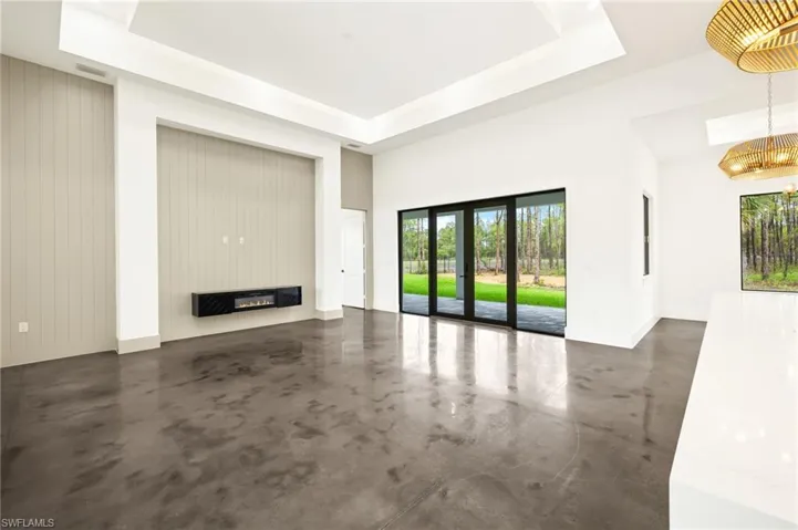 Unfurnished living room featuring a tray ceiling, finished concrete floors, a glass covered fireplace, baseboards, and a notable chandelier
