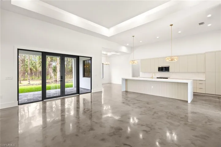 Unfurnished living room with a sink, concrete floors, an inviting chandelier, and a towering ceiling