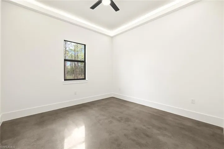 Empty room featuring concrete floors, ceiling fan, a raised ceiling, and baseboards