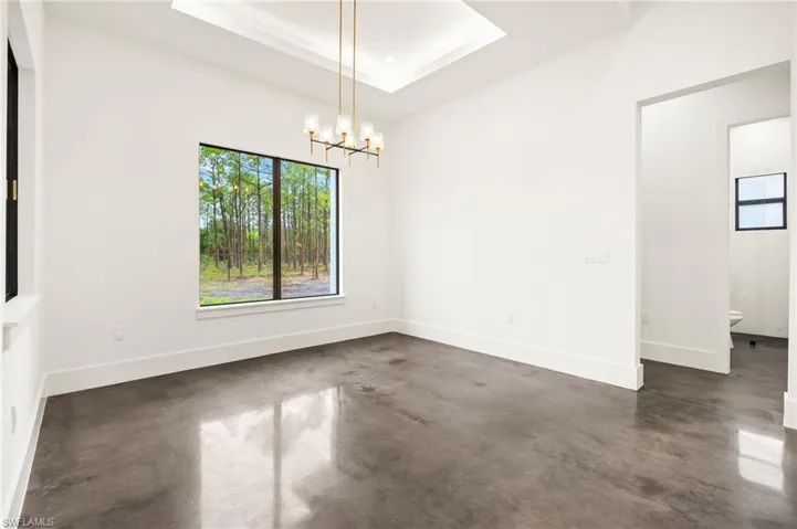 Spare room with a chandelier, finished concrete flooring, baseboards, and a raised ceiling