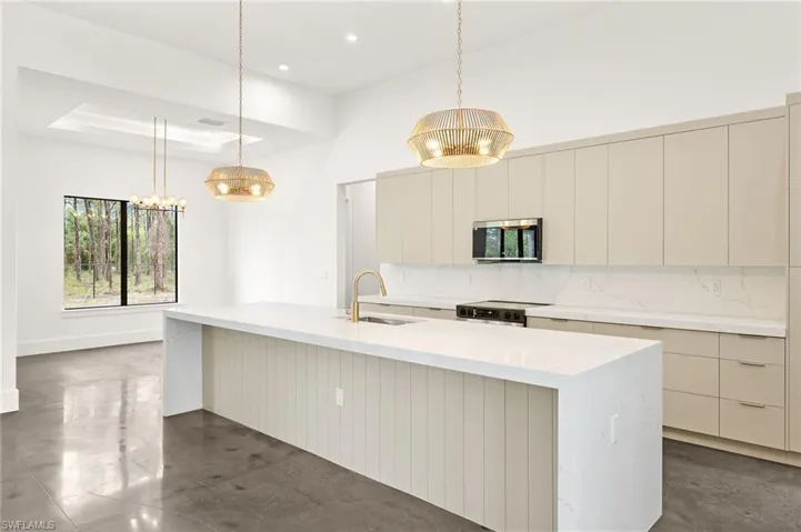 Kitchen featuring appliances with stainless steel finishes, a notable chandelier, a raised ceiling, and modern cabinets