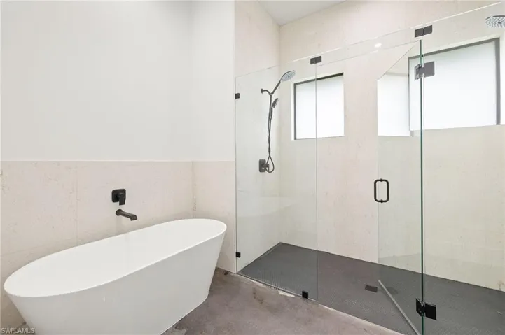 Full bathroom featuring tile walls, a stall shower, a freestanding tub, and concrete floors