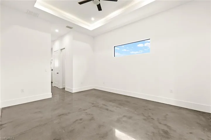 Empty room with visible vents, a tray ceiling, baseboards, and ceiling fan