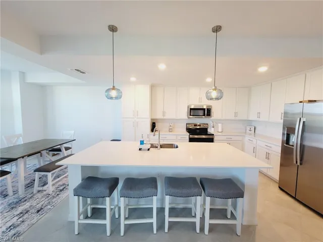 Kitchen with appliances with stainless steel finishes, sink, white cabinetry, hanging light fixtures, and an island with sink