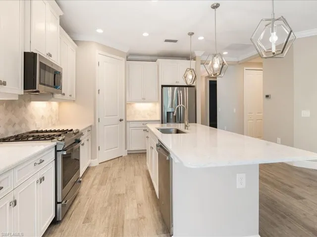 White shaker cabinetry, stainless steel appliances, wood-finish flooring, recessed lighting, and a large kitchen island with pendant lighting