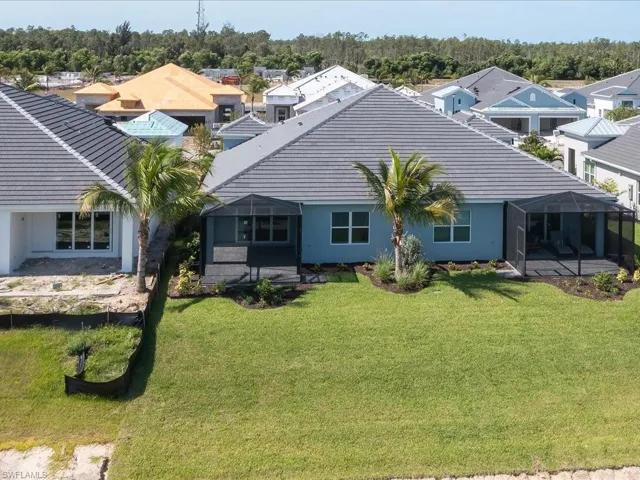 Rear exterior featuring a screened patio, mature landscaping, and a well-maintained lawn