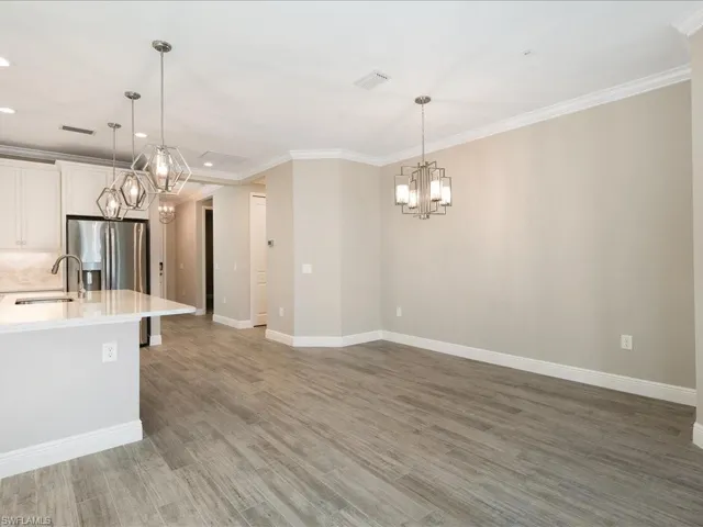 Wood-finish flooring, stainless steel refrigerator, white cabinetry, polished countertop, and decorative pendant lighting