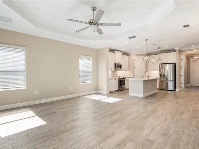Open-concept living area featuring a tray ceiling with a ceiling fan, light wood-finish flooring, and a kitchen with an island, pendant lighting, and stainless steel appliances