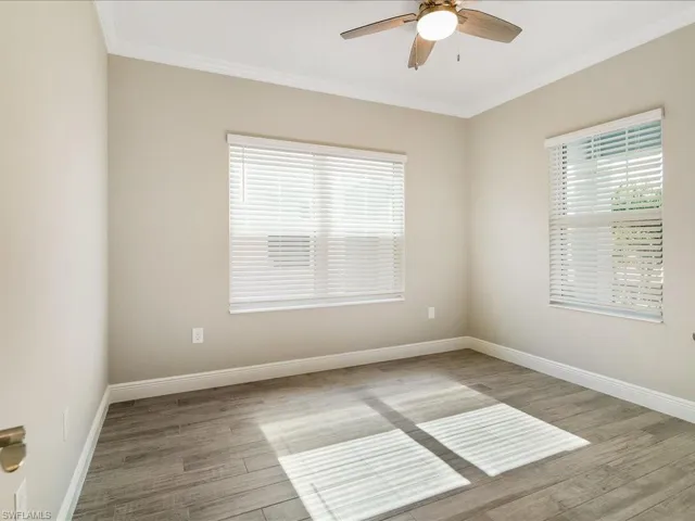 Wood-finish flooring, two windows with blinds, ceiling fan with integrated lighting, and crown molding