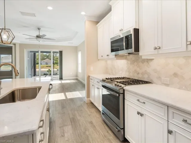 Gourmet kitchen featuring white shaker cabinetry, stainless steel appliances, marble-look countertops, and a decorative tile backsplash