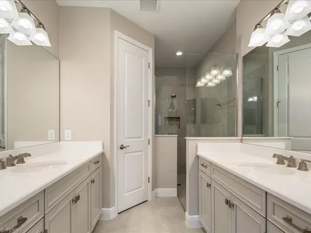 Dual vanities with white countertops, a tiled walk-in shower with glass enclosure, and modern light fixtures