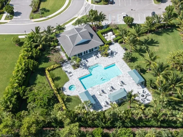 Clubhouse building with a multi-level roofline, large swimming pool, integrated spa, expansive paver patio, and lush landscaping