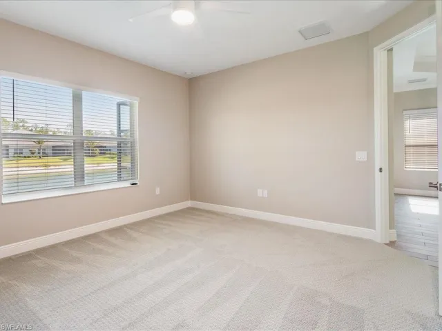 Plush carpeted flooring, a ceiling fan with integrated lighting, and a large window with blinds