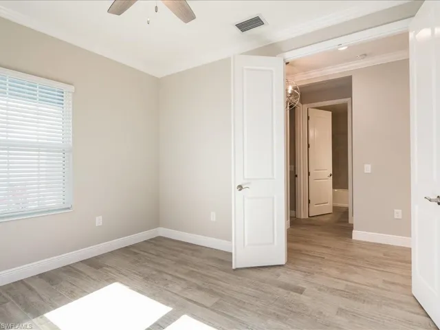Wood-finish flooring, ceiling fan, crown molding, white trim, and a window with blinds