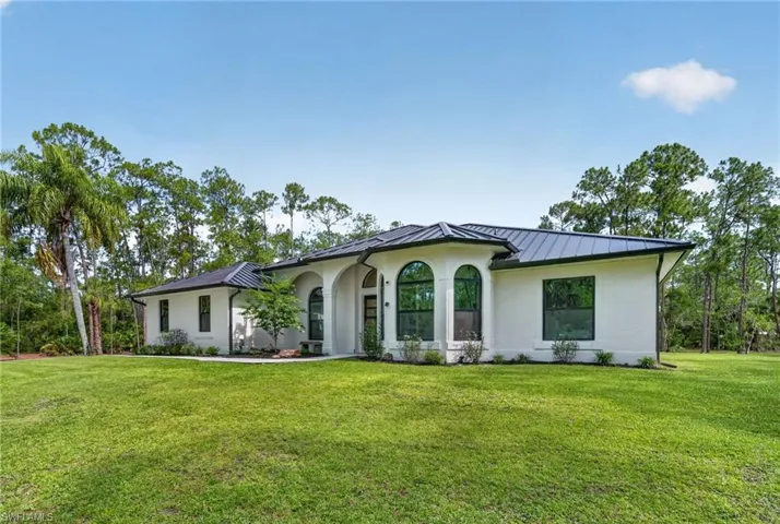 White brick exterior featuring a dark metal roof, arched windows, and a manicured lawn