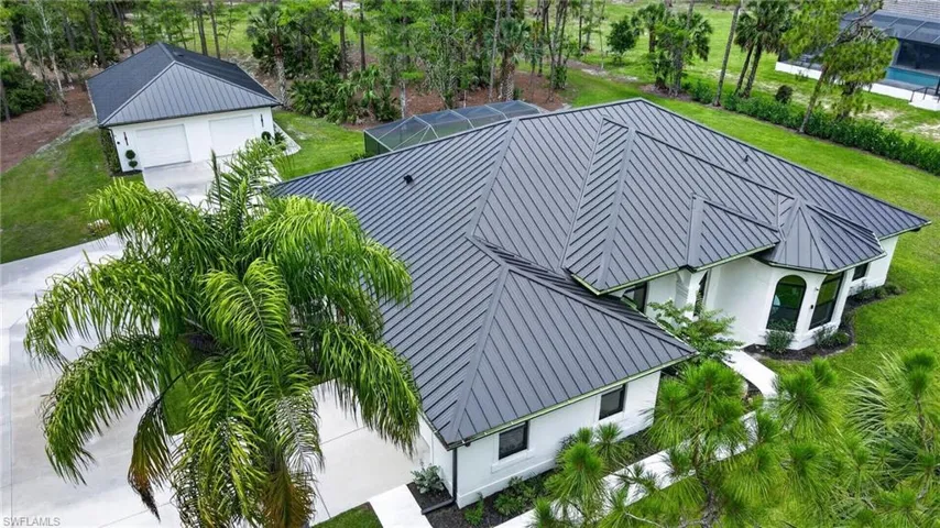 Contemporary residence featuring a dark metal roof, white stucco exterior, multiple arched windows, and lush green landscaping
