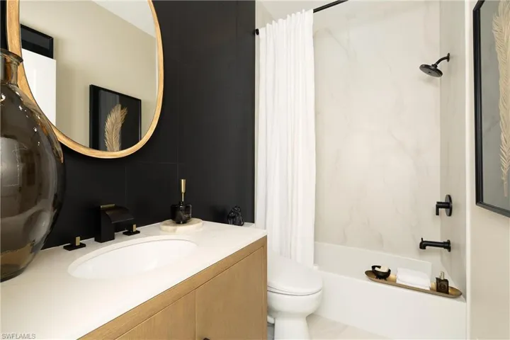 Contemporary bathroom featuring a wood-finish vanity with an integrated sink, matte black fixtures, and a gold-framed mirror