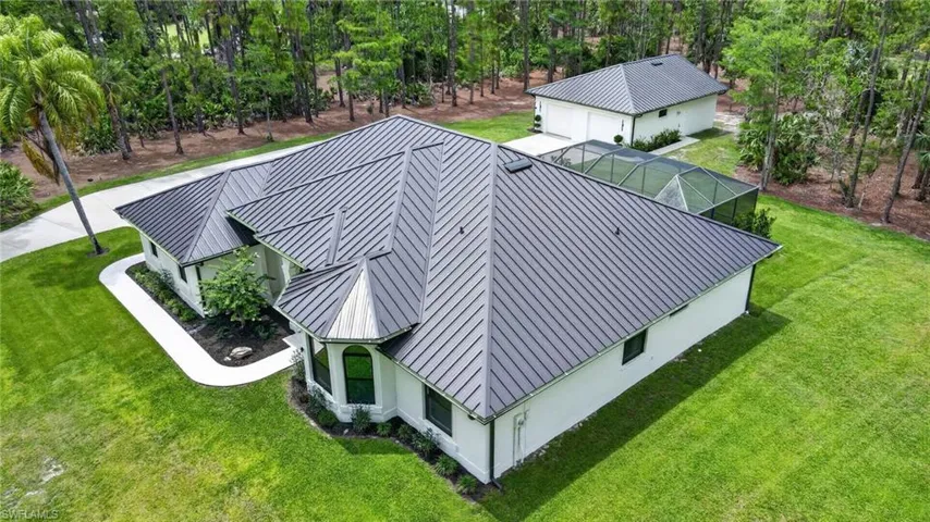 Expansive property featuring a main residence with a dark metal standing seam roof, a detached auxiliary building, and a screened enclosure