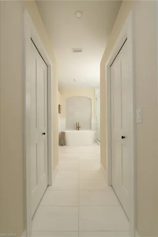 Hallway featuring recessed lighting, paneled doors, and large format tile flooring, leading to a freestanding soaking tub with a tiled accent wall