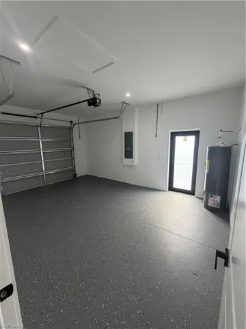 Spacious garage featuring a finished epoxy floor, an overhead garage door with opener, a side entry door, and recessed ceiling lighting