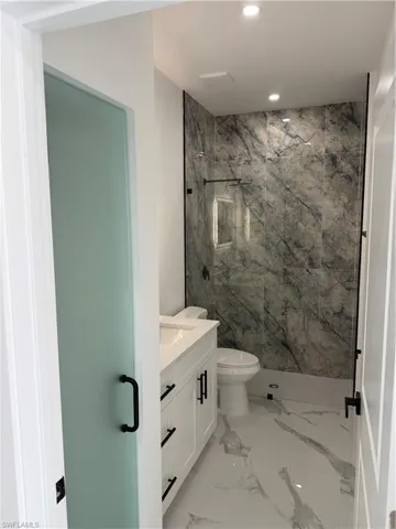 Contemporary bathroom featuring a floating white vanity with a quartz countertop, a walk-in shower with large format marble-look wall tiles, and contrasting black hardware