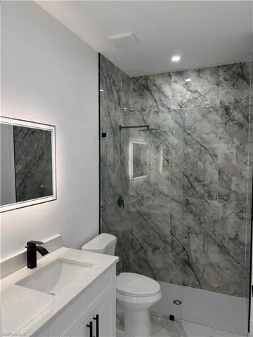 Contemporary bathroom featuring a spacious walk-in shower with large-format marbled tile, a frameless glass enclosure, a matte black rainfall shower head, and a built-in shower niche