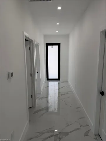 Hallway with polished tile flooring, recessed ceiling lighting, crisp white walls, and contemporary black door frames