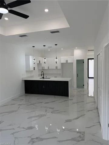 Open-concept living area featuring large format polished tile flooring, a kitchen island with a fluted black base and white countertop, white shaker cabinetry, and contemporary pendant lighting
