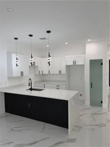 Modern kitchen featuring a waterfall island with a black fluted panel base, white shaker cabinetry, quartz countertops, and three contemporary pendant lights