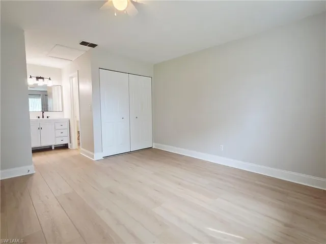 Unfurnished bedroom featuring light wood-type flooring, a closet, a ceiling fan, and ensuite bath