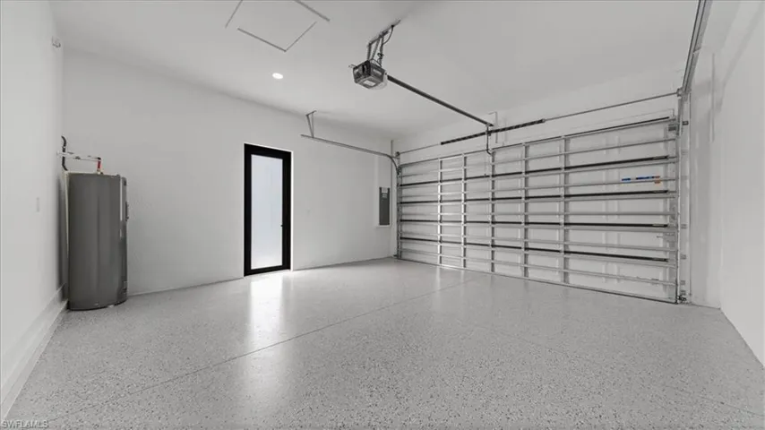 Garage with water heater, electric panel, a garage door opener, and recessed lighting