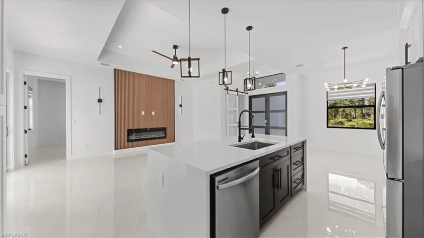 Kitchen with a tray ceiling, appliances with stainless steel finishes, a large fireplace, light stone countertops, and decorative light fixtures