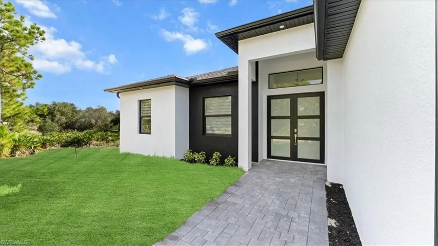 View of exterior entry with stucco siding and a lawn
