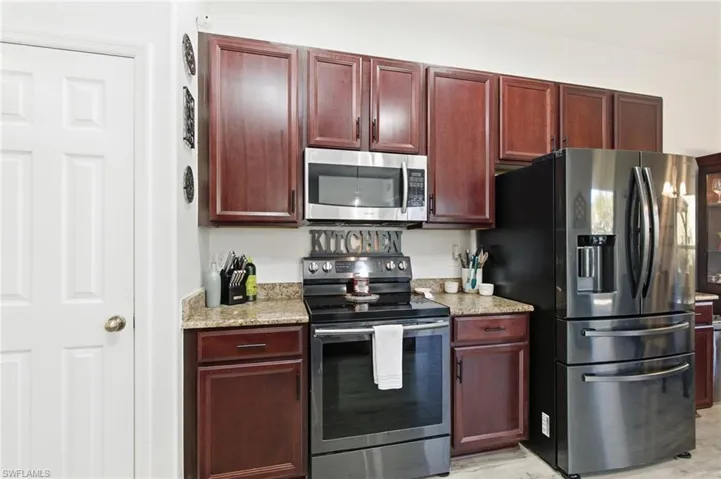 Kitchen with appliances with stainless steel finishes, dark brown cabinets, and light stone counters