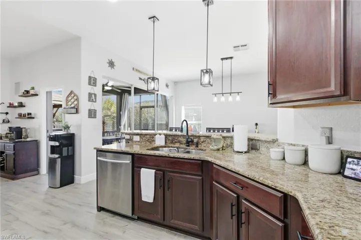 Kitchen with a peninsula, pendant lighting, stainless steel dishwasher, light stone countertops, and light wood-style flooring