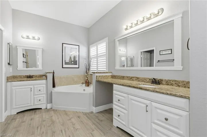 Full bath with two vanities, light wood-style flooring, and a bath