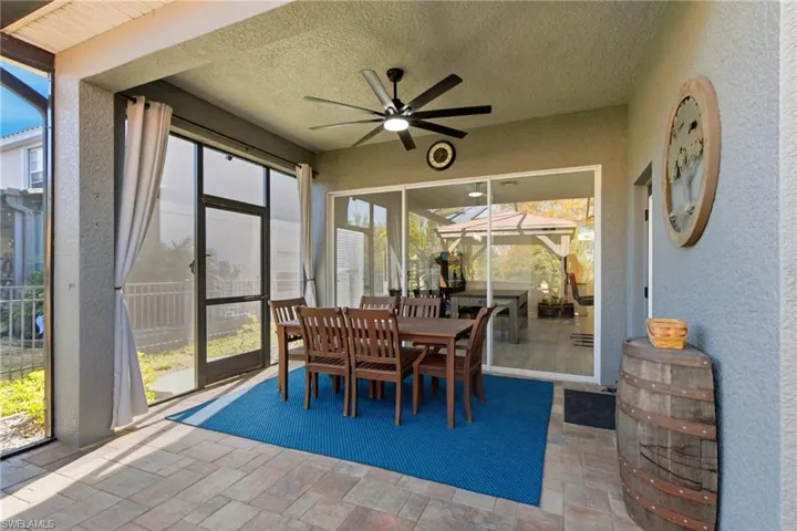 Sunroom / solarium featuring a textured wall, a ceiling fan, stone tile floors, outdoor dining area, and a patio