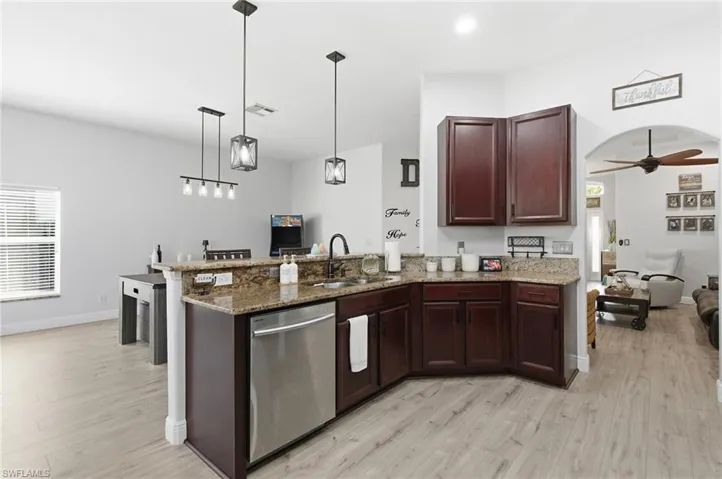 Kitchen with dark stone counters, dishwasher, a peninsula, ceiling fan, and light wood-type flooring