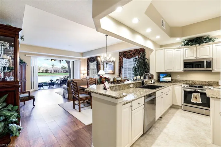 Kitchen with light stone countertops, stainless steel appliances, a peninsula, and white cabinetry