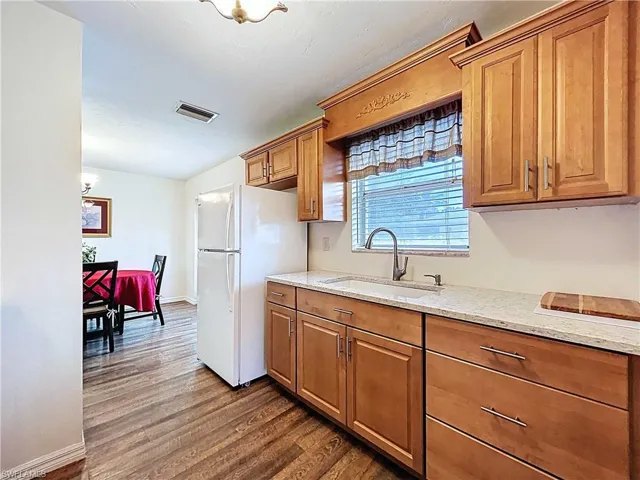 Kitchen featuring light stone countertops, freestanding refrigerator/freezer, brown cabinetry.Nice bright kitchen with window over the sink