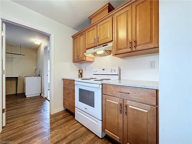 Updated kitchen with white electric range, under cabinet range hood, brown cabinetry, and light stone counters