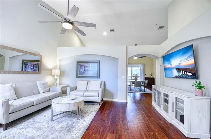 Living room featuring a ceiling fan, arched walkways, high vaulted ceiling, dark wood-style floors, and baseboards