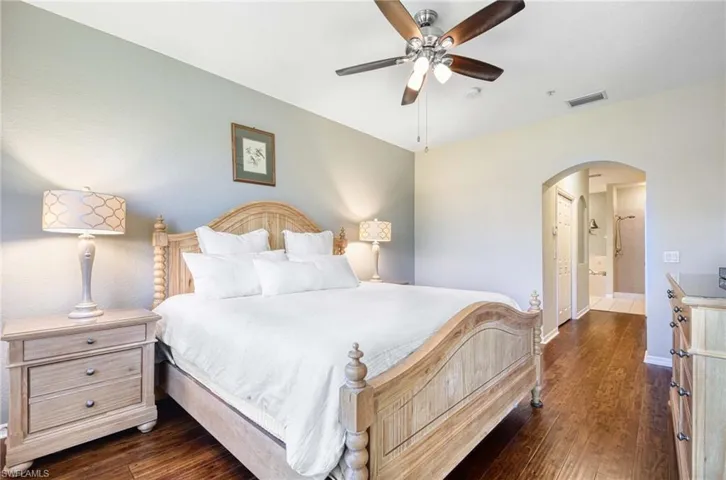 Bedroom with arched walkways, dark wood finished floors, baseboards, and ceiling fan