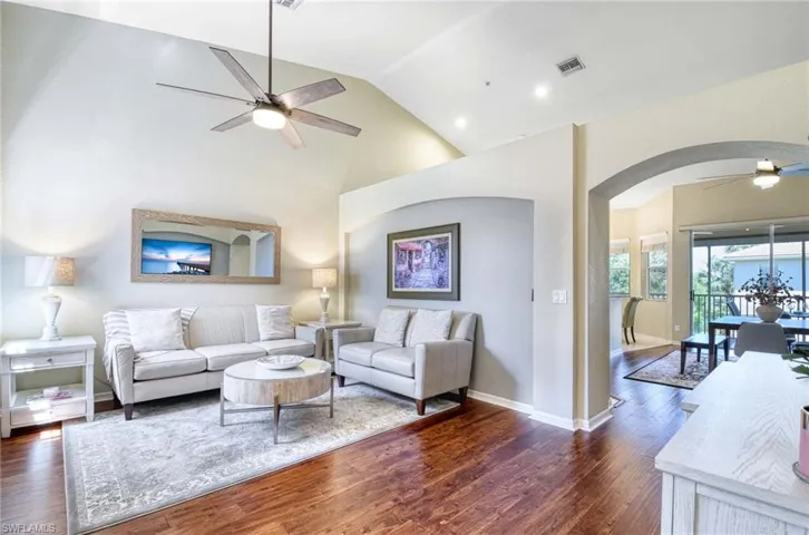 Living area featuring ceiling fan, arched walkways, dark wood-style flooring, high vaulted ceiling, and baseboards